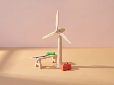 Une éolienne en pâte, une pale posée sur un tréteau à côté d’une pilule verte, une caisse à outils rouge au pied du mât.