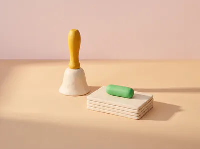 Une clochette crème à manche jaune en pâte, à côté d’une pile de cartes surmontée d’une pilule verte.